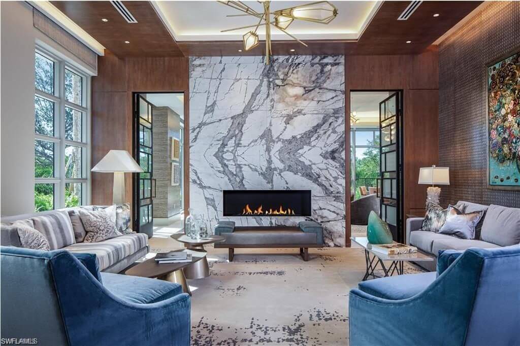 Floor to ceiling fireplace, blue soft chairs, two couches, very luxurious